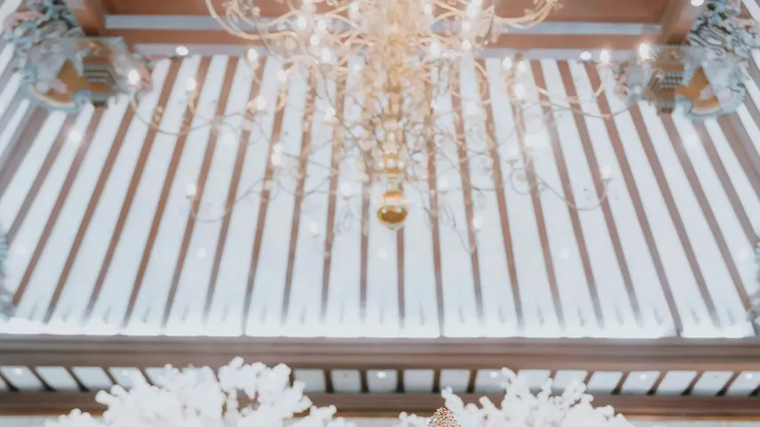 Chandelier under a carved joglo ceiling above white blossom trees
